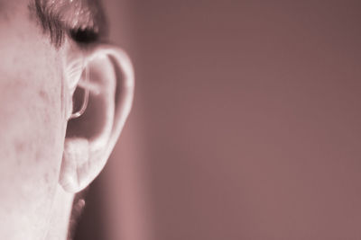 Close-up of person wearing hearing aid against colored background
