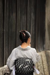 Rear view of woman in kimono standing by wall