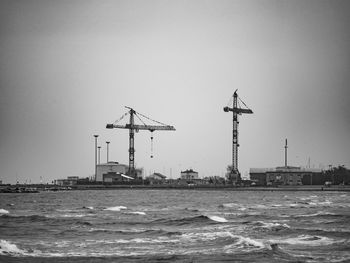 Cranes by sea against clear sky