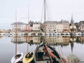 Sailboats moored on canal by buildings in city against sky