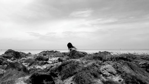 Woman on rocky shore against sky