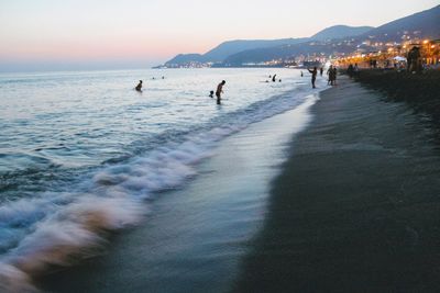 People enjoying at beach against sky during sunset