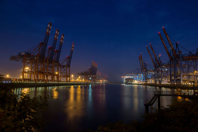 Illuminated cranes at dock against sky at night