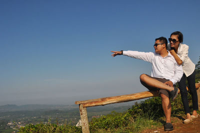 Couple sitting on cliff against clear sky