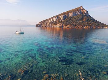 Idyllic shot of sailboat in sea with island against sky