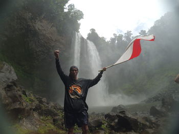 Portrait of woman with arms raised standing against waterfall