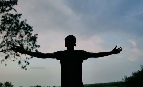 Rear view of man with arms raised standing against sky