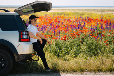 Side view of man by suv car on multi coloured poppy field in summer
