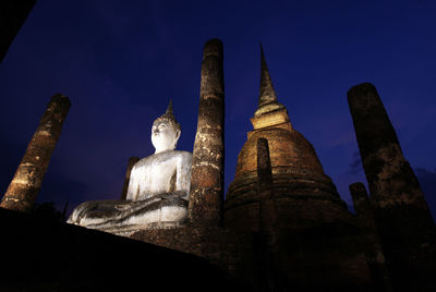 Low angle view of buddha statue and temple against sky at night