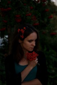 Portrait of a beautiful young woman standing by red flowering plants