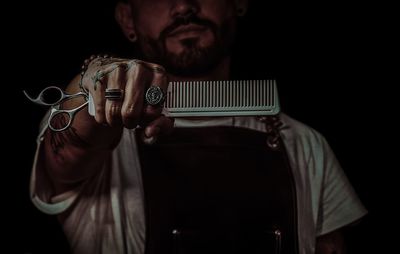 Midsection of man holding scissor while standing against black background