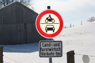 Sign board by fence against log cabin on snow covered field