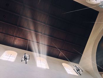 Low angle view of lighting equipment hanging from wooden ceiling in church