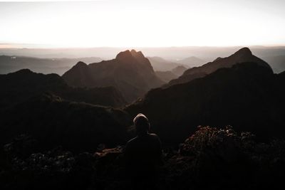 Rear view of sad man looking sunset at mountain range against sky