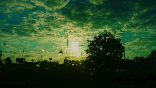 Silhouette electricity pylon against cloudy sky
