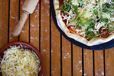 Vegetable pizza next to a wooden rolling pin and shredded cheese.