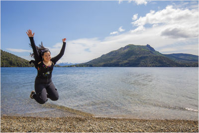 Full length of woman jumping on shore at beach against sky