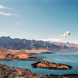 People paragliding over sea against mountains and sky