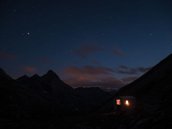 Tent by silhouette mountains against star field in sky at night