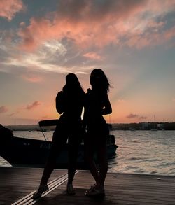 Silhouette females standing by sea against sky during sunset