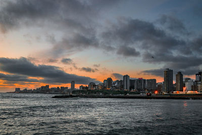 Sea by buildings against sky during sunset
