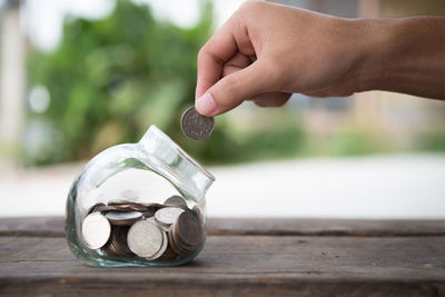 Close-up of person putting coin in jar on table