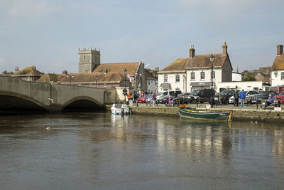 Bridge over river by buildings against sky