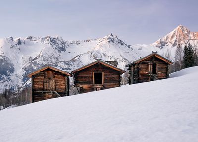 Wooden houses on snowcapped mountain against clear sky