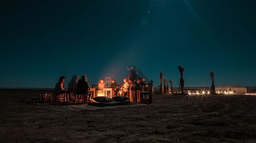 People relaxing on beach against sky at night