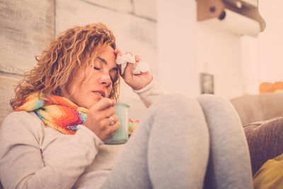 Close-up of sick woman holding coffee cup resting at home