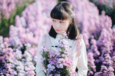 Beautiful woman looking away while standing by purple flowering plants