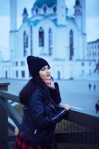 Young woman looking away while standing on railing in city
