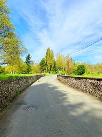 Empty road along plants and trees against sky