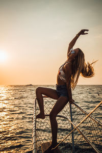 Woman with umbrella in sea against sky during sunset