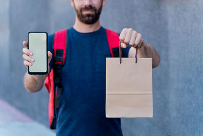 Midsection of delivery person holding cardboard bag with mobile phone