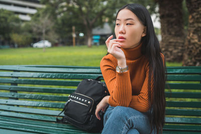 Young woman looking away while sitting on bench