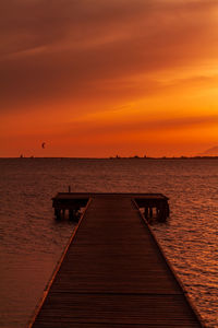 Wooden pier over sea against orange sky