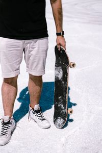 Low section of man holding skateboard while standing on floor