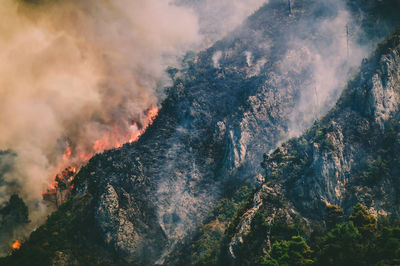 Smoke emitting from mountain against sky