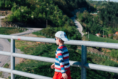 Boy walking on bridge against trees in city