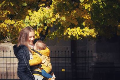 Portrait of young woman using carrying the toddler under yellow leaves 
