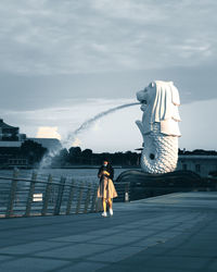 Rear view of woman standing by fountain in city against sky