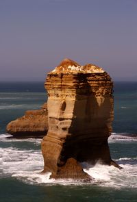 Rock formation by sea against clear sky