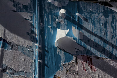 Full frame shot of wall with torn posters during sunny day