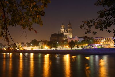 Illuminated buildings by river against sky at night