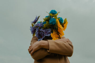 Person covering face with bouquet against clear sky