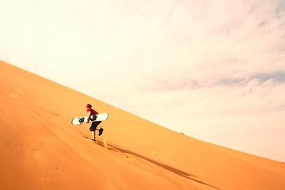 Man with surfboard on sand against sky