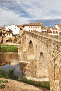 Arch bridge over river against cloudy sky