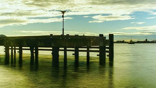 Pier on sea against cloudy sky