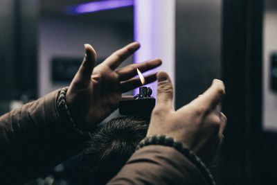 Cropped hand of person gesturing around cigarette lighter on mans head